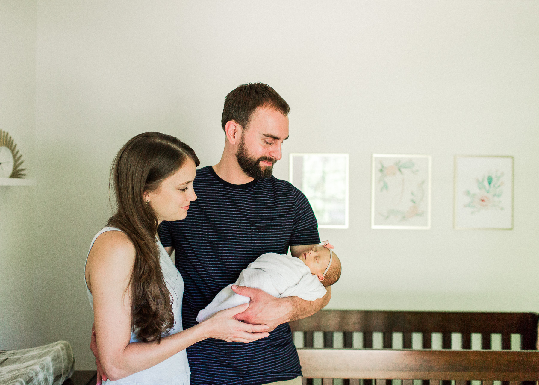 mama and daddy standing close near crib admiring baby